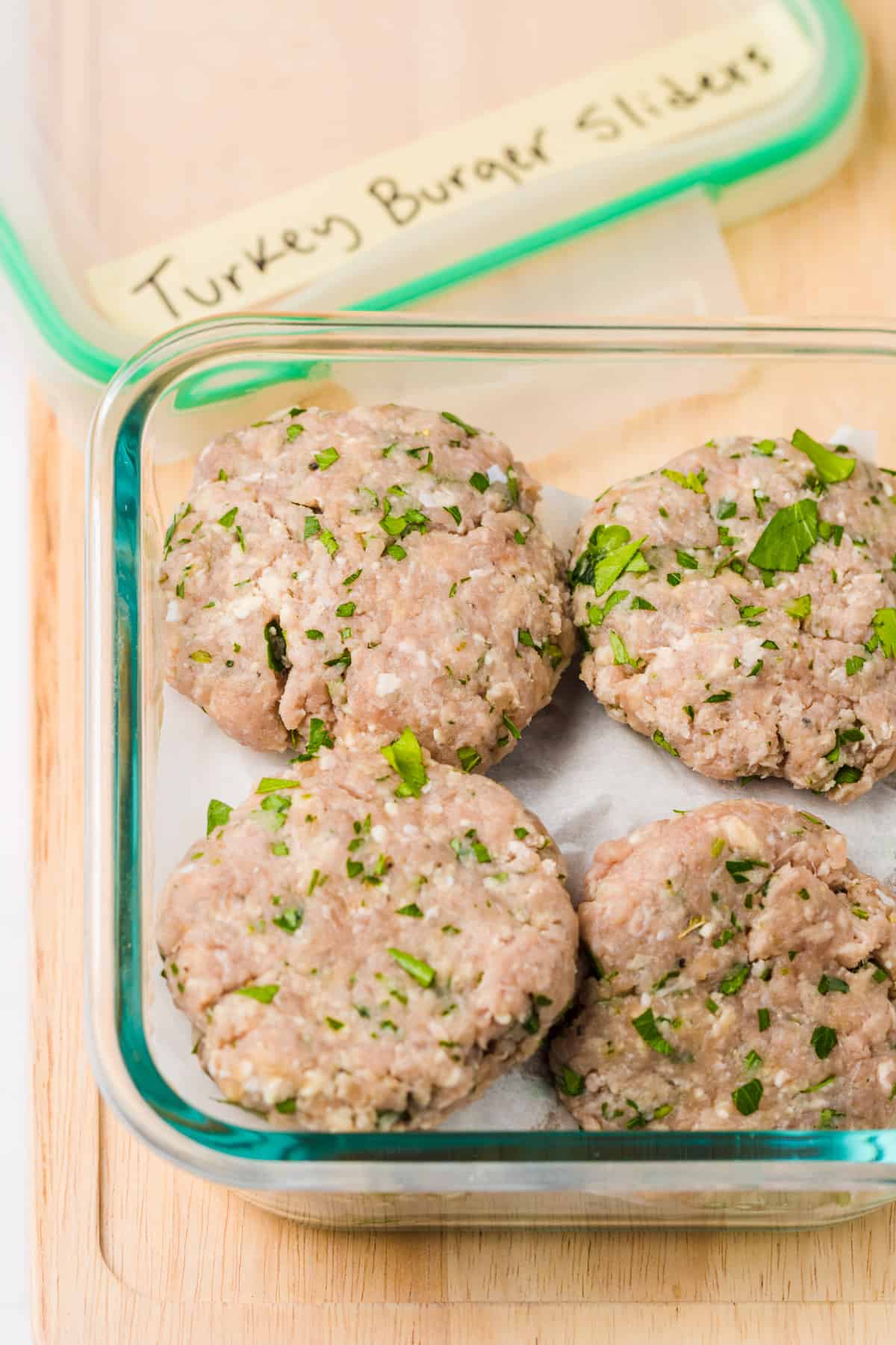 Turkey burger sliders prepped and placed on parchment paper in a freezer container.