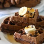 Chocolate zucchini waffles stacked on a plate and topped with banana slices, peanut butter, and mini chocolate chips.