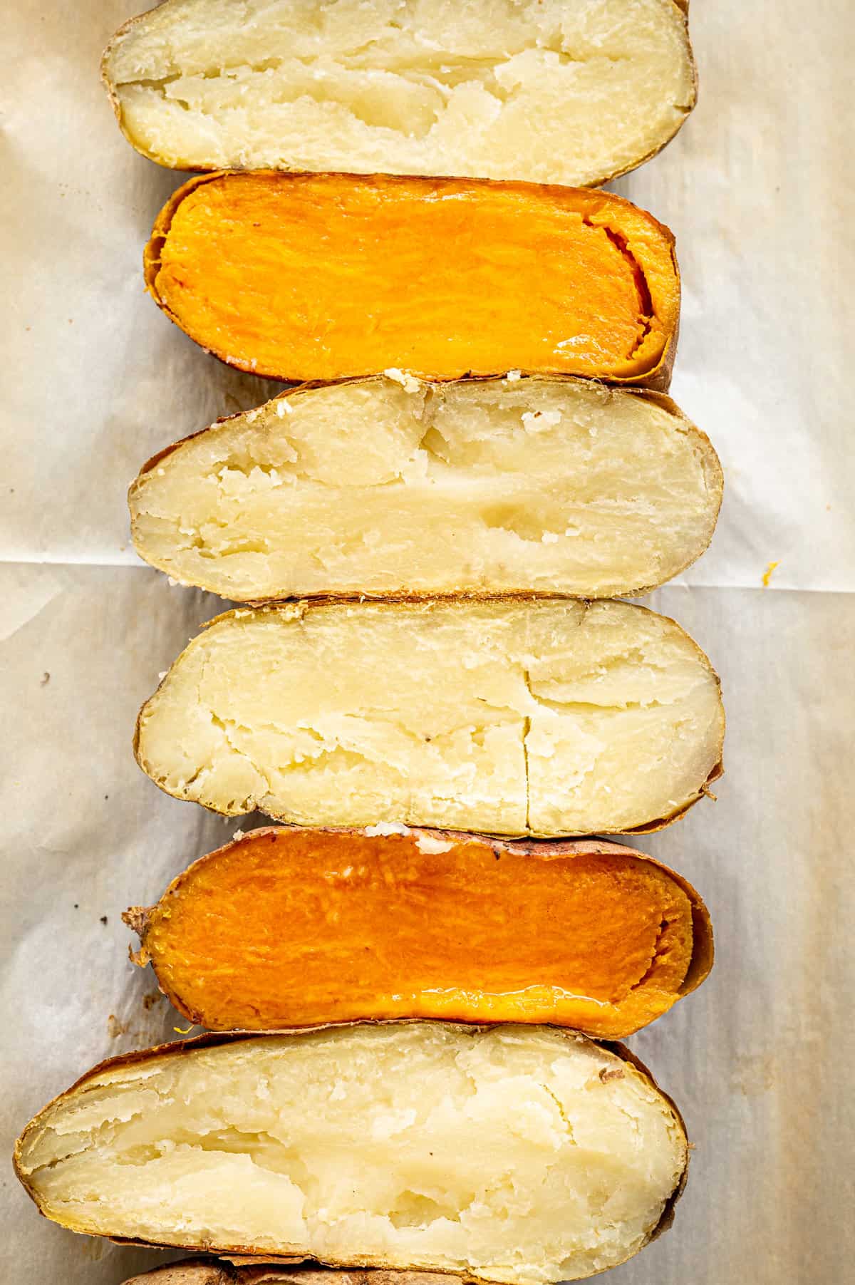 Baked Russet and sweet potatoes  cut in half long ways laid out on parchment lined baking sheet.