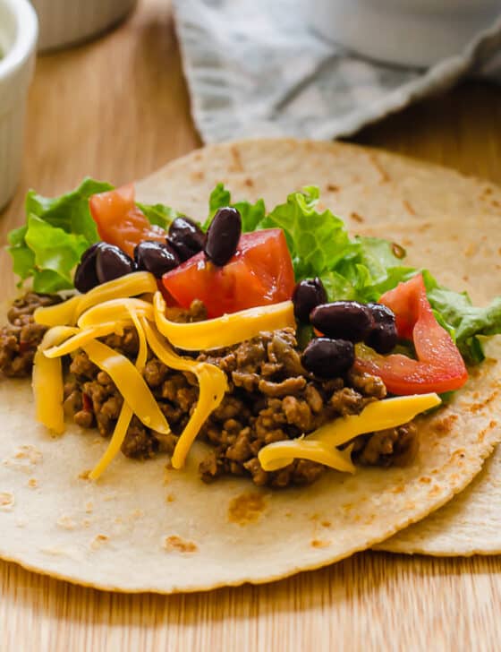 Taco meat in a soft taco with chopped tomatoes and lettuce and shredded cheese on top.