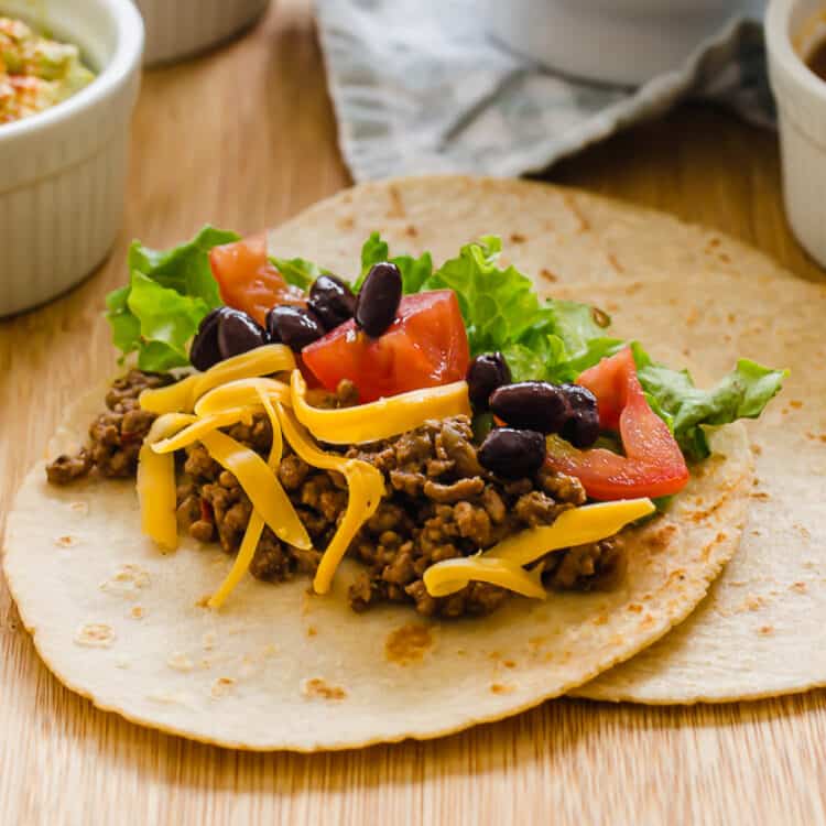 Taco meat in a soft taco with chopped tomatoes and lettuce and shredded cheese on top.