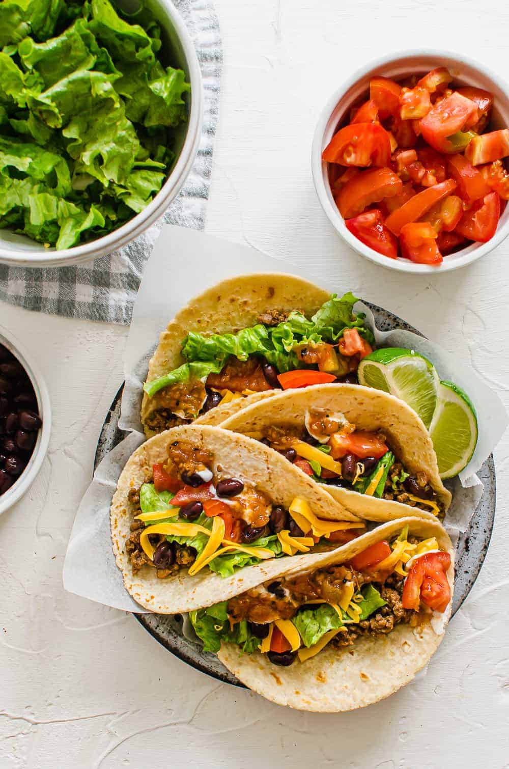 Ground Beef Tacos on a tray with tomatoes and lettuce in bowls on the side.
