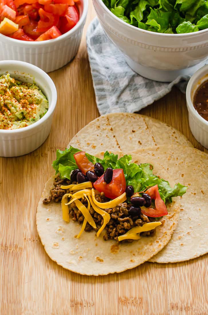 Taco meat on a taco with toppings in the background.