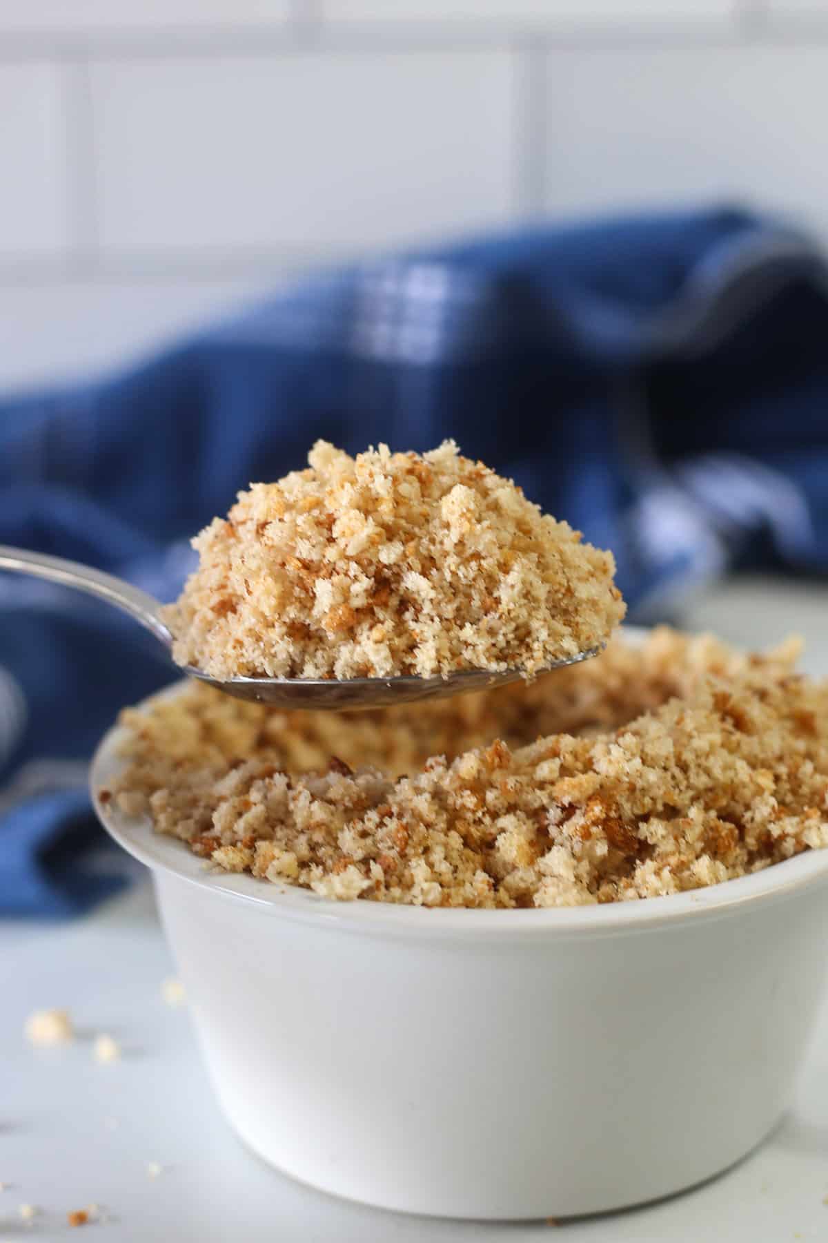 A spoonful of gluten-free breadcrumbs being scooped out of a bowl.