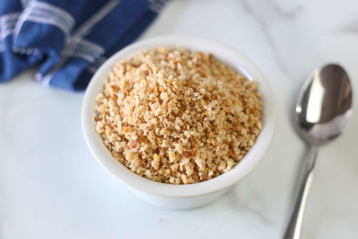 Homemade bread crumbs in a white bowl with a spoon beside it.