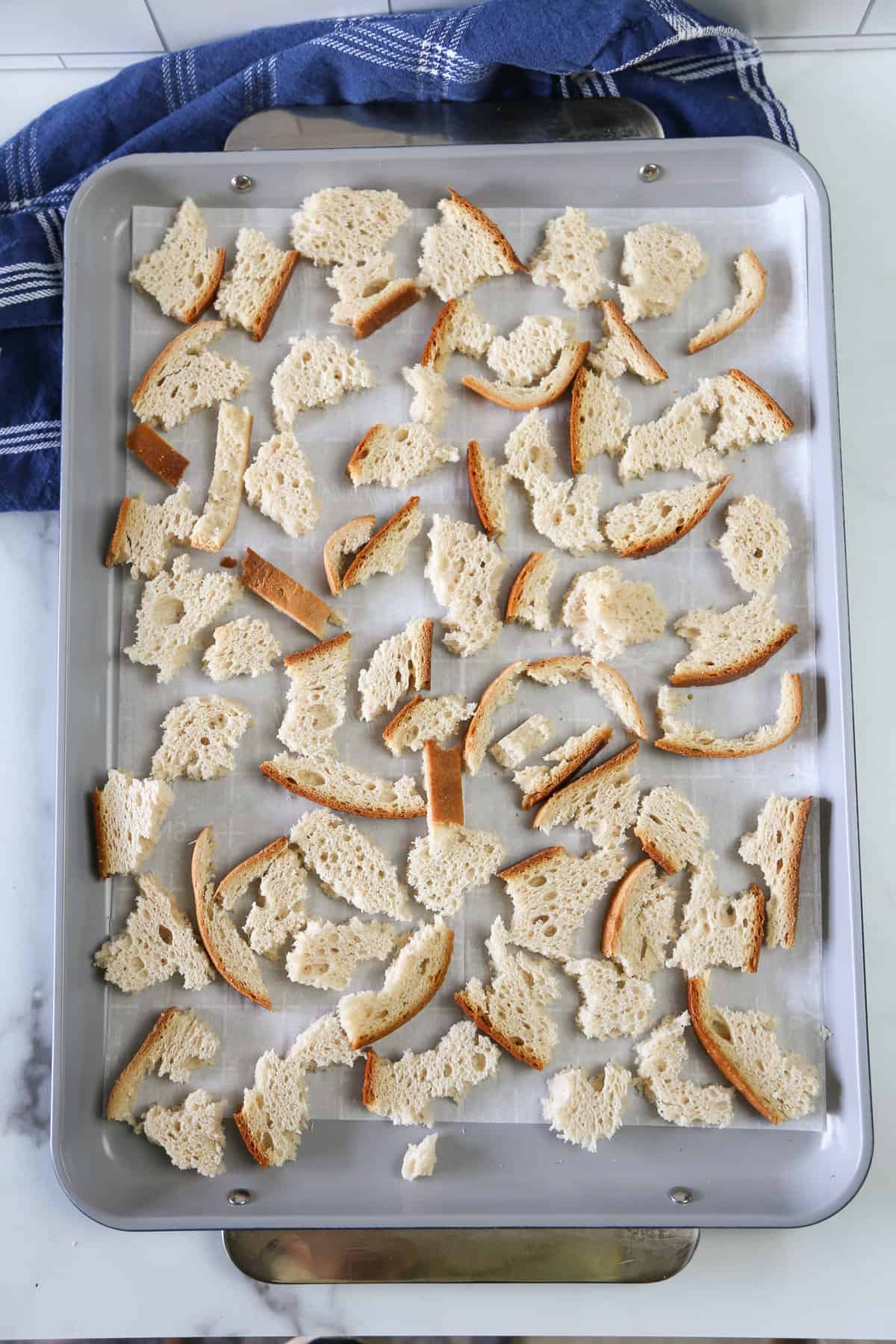 Torn up pieces of bread on a parchment lined baking sheet that have been baked.
