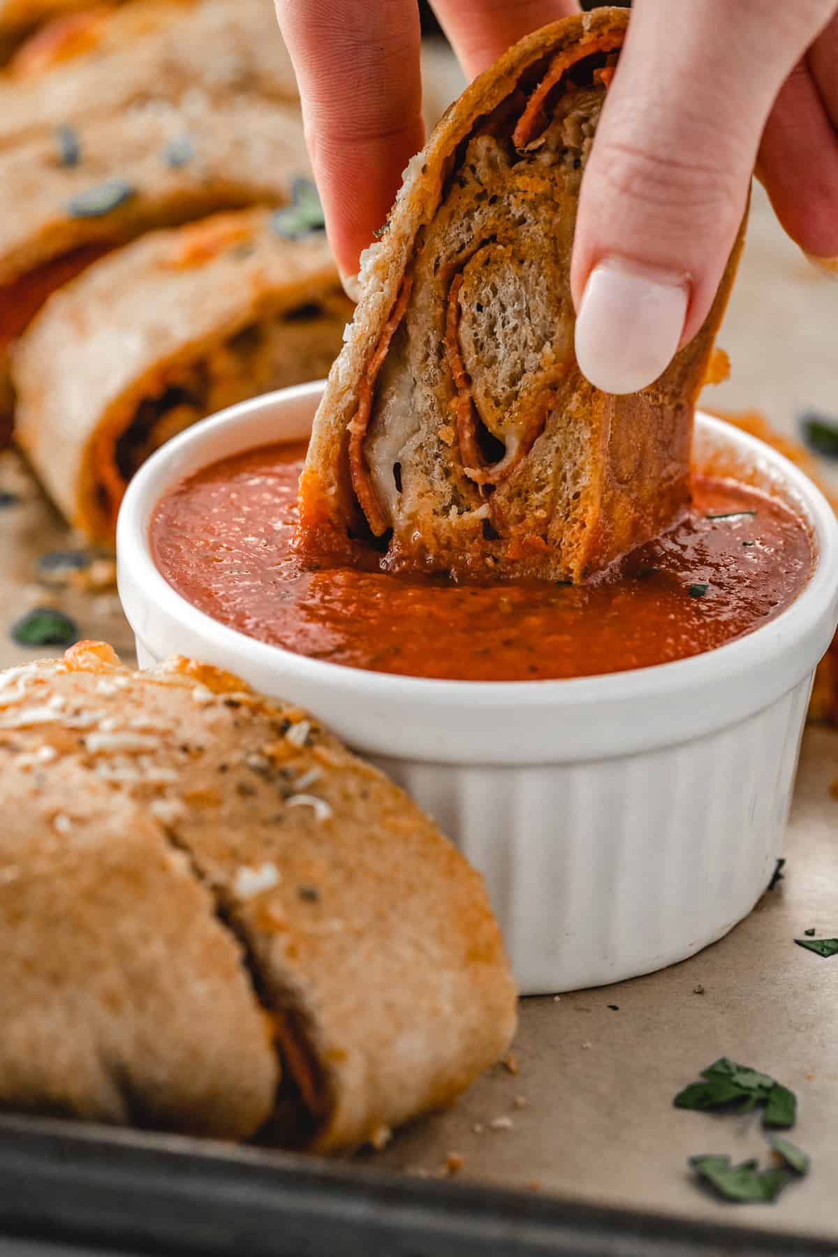 Hand dipping a slice of stromboli pizza into a ramekin of marinara sauce.