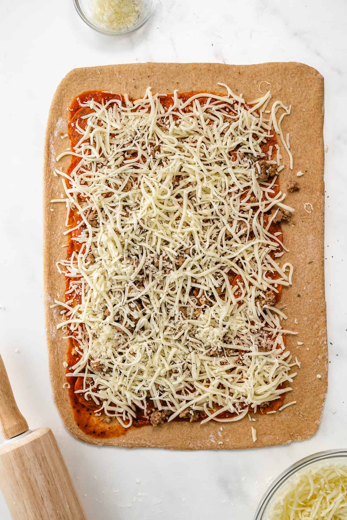 A rectangle of pizza dough covered with pizza sauce, pepperoni, and shredded mozzarella.