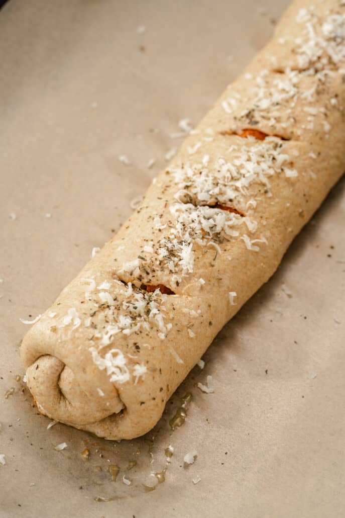 Rolled up stromboli pizza with slits cut on top and grated parmesan and spices on top before baking