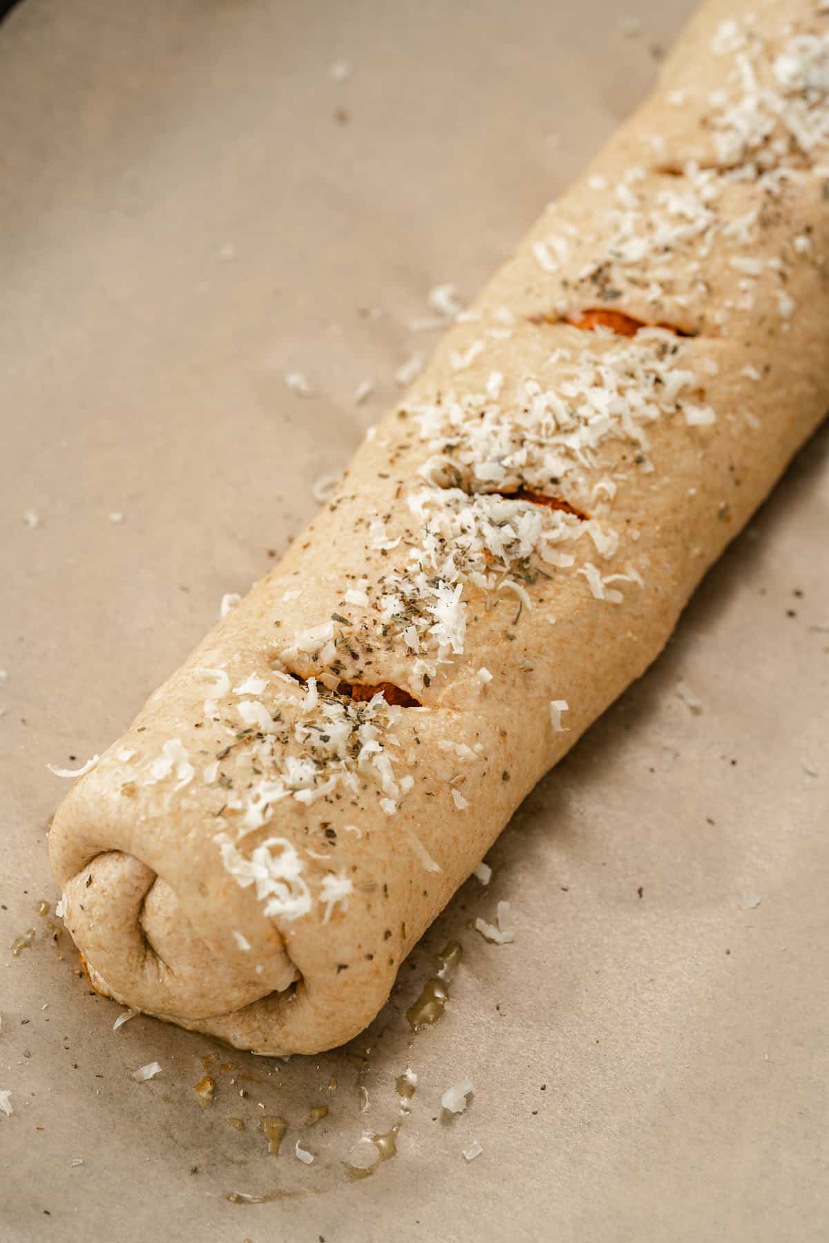 Rolled up stromboli pizza with slits cut on top and grated Parmesan on top before baking.