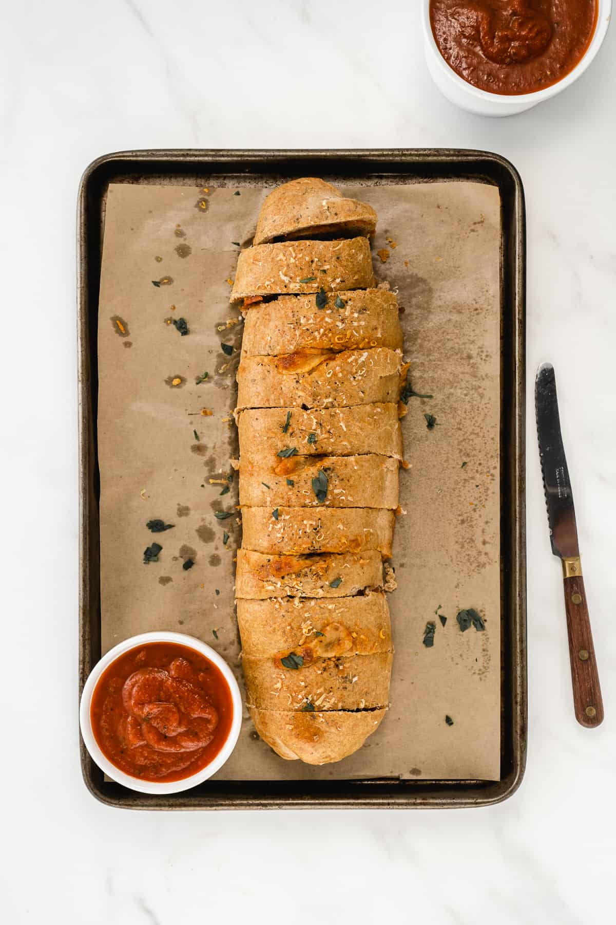 Sliced Stromboli Pizza on a parchment-lined baking sheet with marinara on the side.