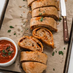 Sliced Stromboli Pizza on a baking sheet with marinara and chopped fresh parsley.