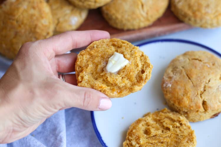 A hand holding a sweet potato biscuit that is buttered.