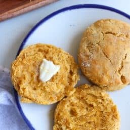 Sweet potato biscuits on a plate with one buttered.