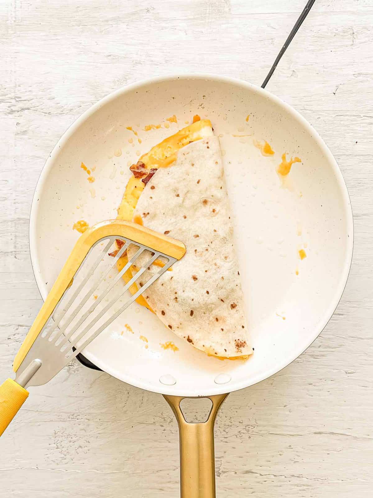 Breakfast Quesadilla being made by folding tortilla in half on to eggs and cheese.