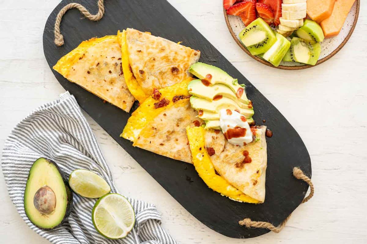 A Breakfast Quesadilla cut in triangles on a serving tray with sliced avocado and a dollop of sour cream. 