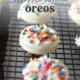 White chocolate covered Oreos with sprinkles on top on a cooling rack.