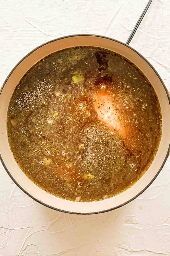 chicken breast in broth in pot with seasonings