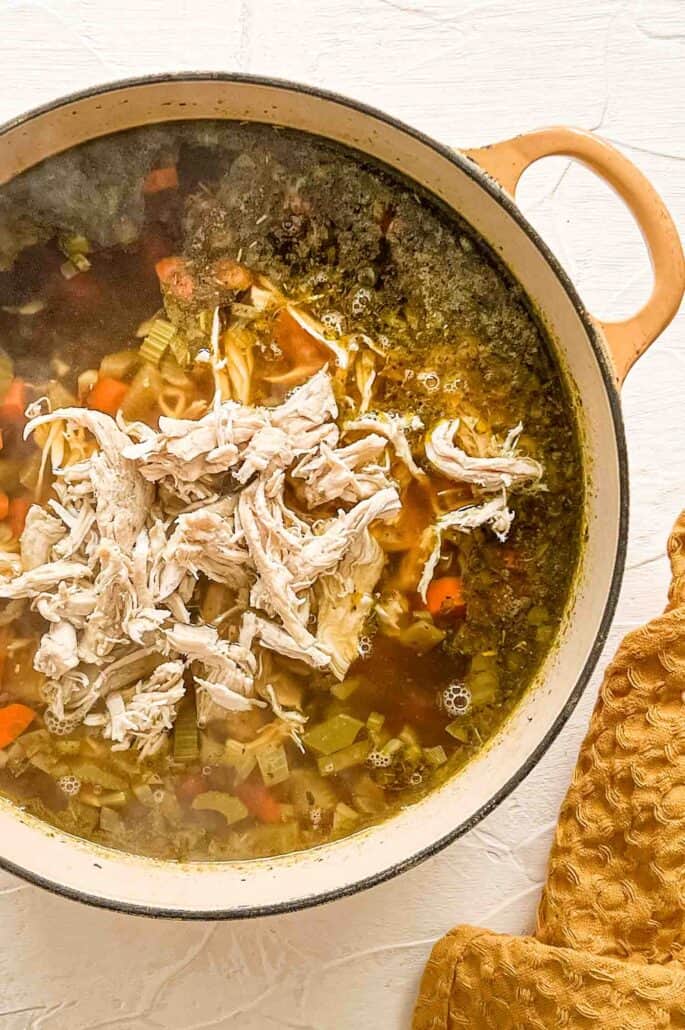 shredded chicken at the top of a pot of broth, veggies and seasonings before being stirred in