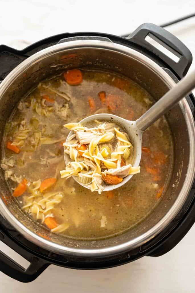 Ladle of Instant Pot Chicken Noodle Soup held above the Instant Pot with soup