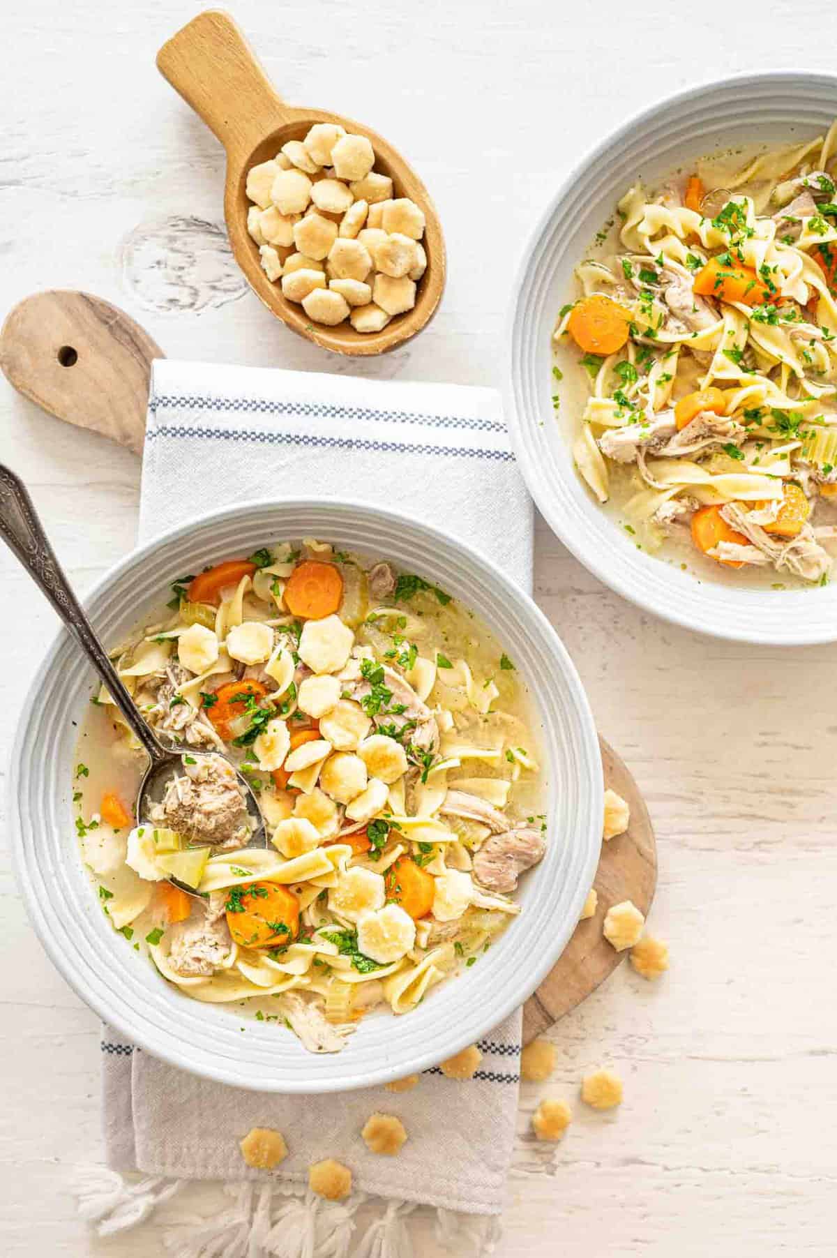 Two bowls of Chicken Noodle Soup with oyster crackers in and around the bowls.