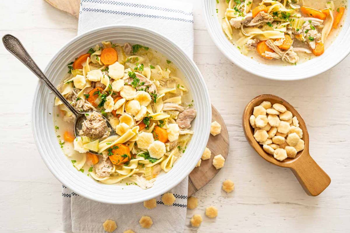 Bowls of Chicken Noodle Soup with Oyster Crackers in and around the bowls.