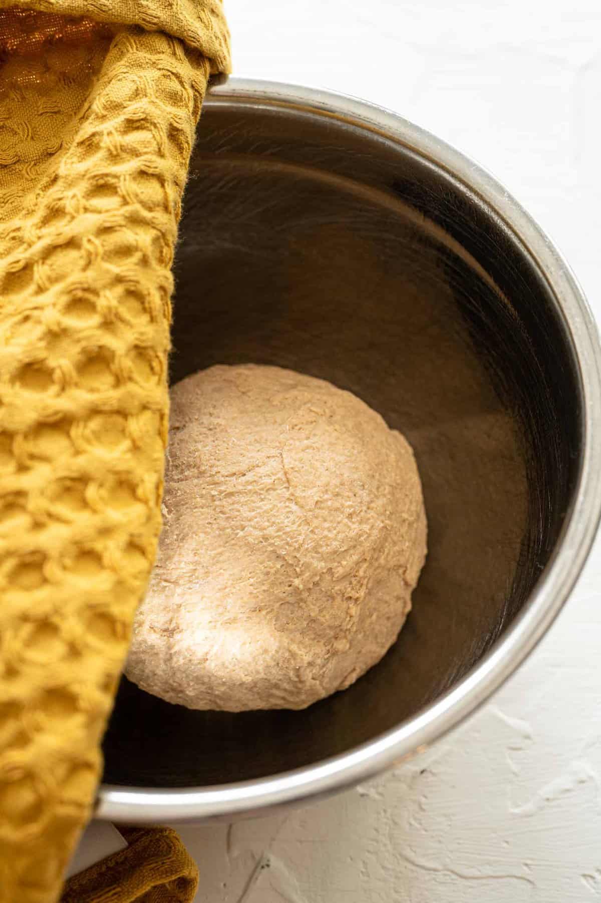 Calzone dough in a bowl about to be covered with a towel so it can rise.