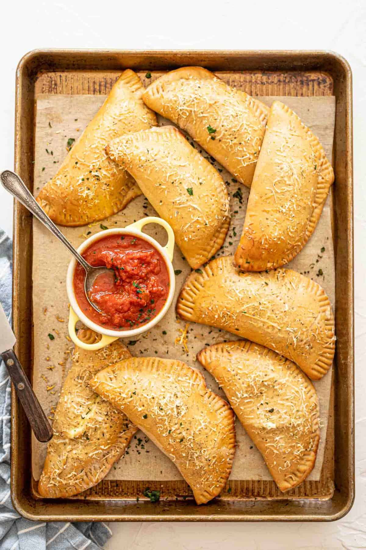 Calzones on baking sheet after being baked with Parmesan and parsley sprinkled on top.