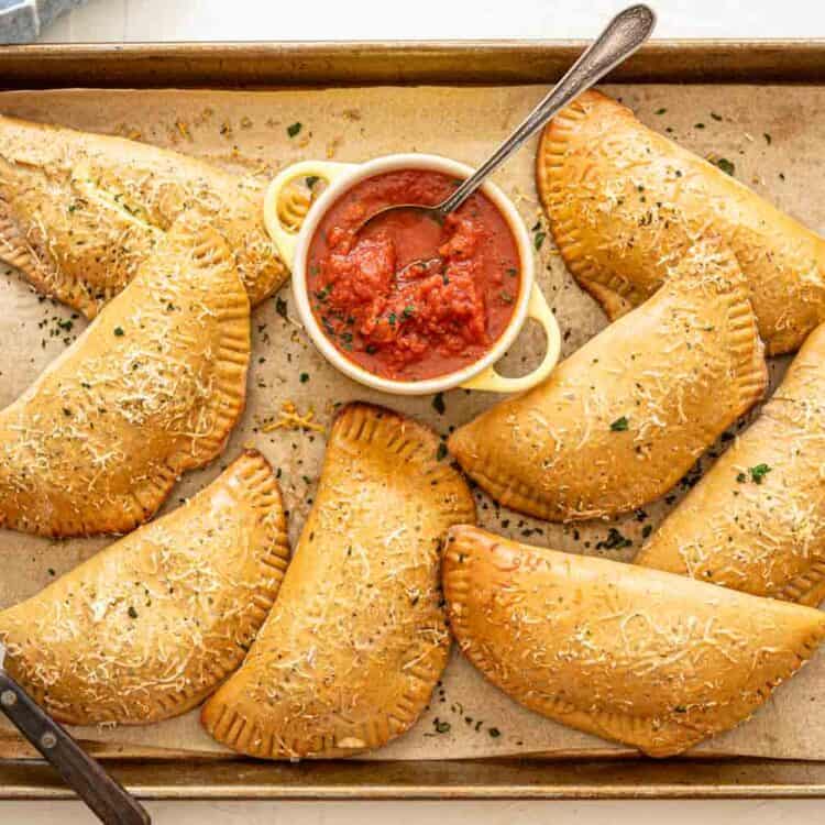 Calzones on baking sheet after being baked with Parmesan and parsley sprinkled on top.