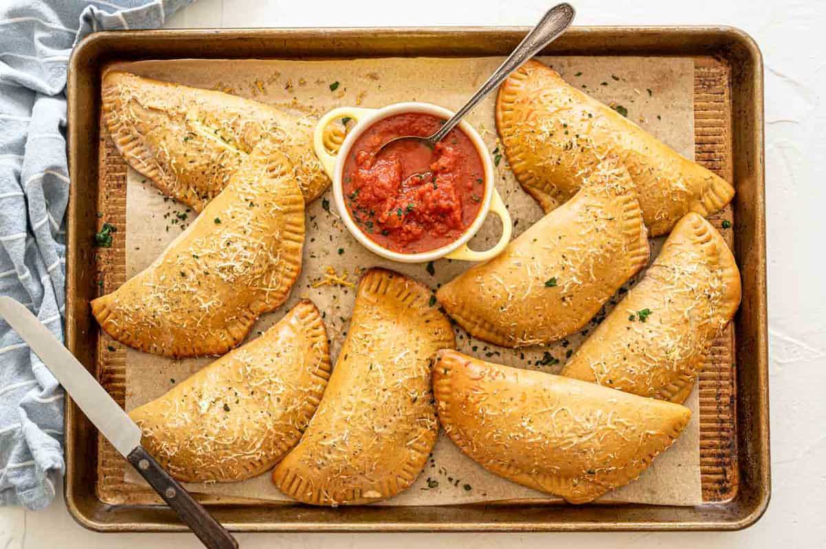 Calzones on baking sheet after being baked with parmesan and parsley sprinkled on top