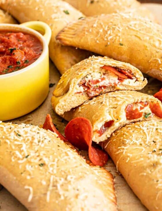 Pepperoni Calzones after baking piled on baking sheet with one cut open to see the cheesy insides with pepperoni slices as well