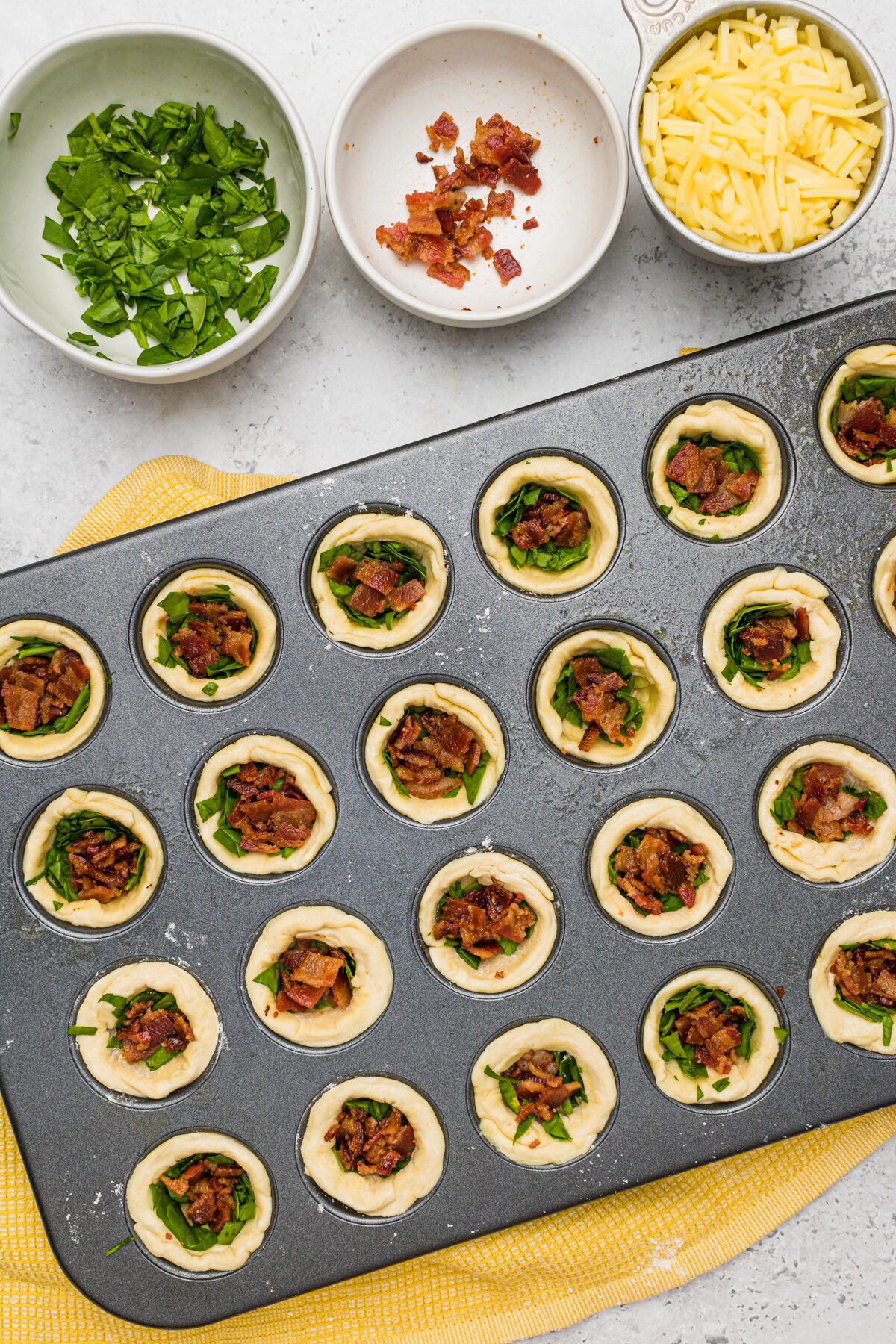 Mini muffin pan with pie crust pushed in with bacon, spinach on top. 