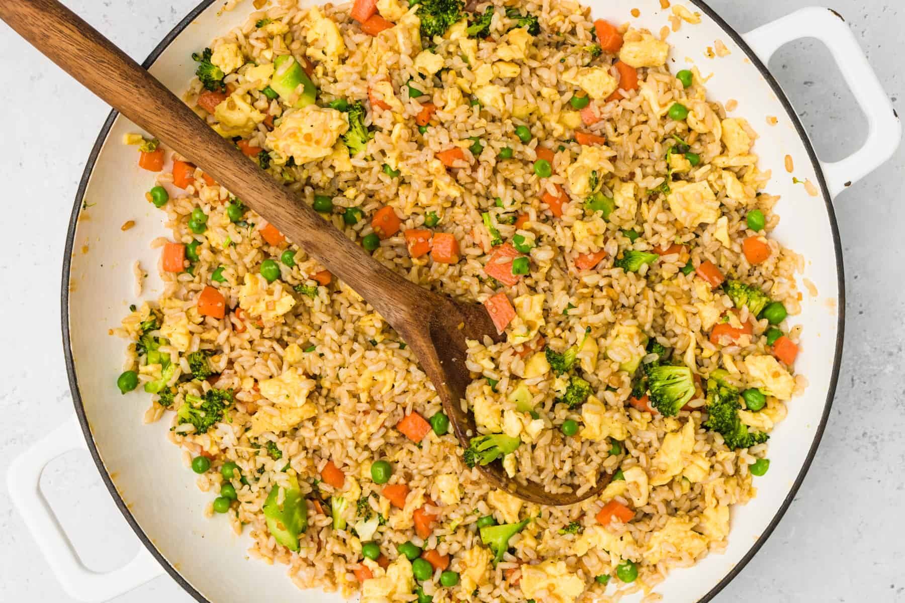 Skillet of egg fried rice with wooden spoon ready to serve.