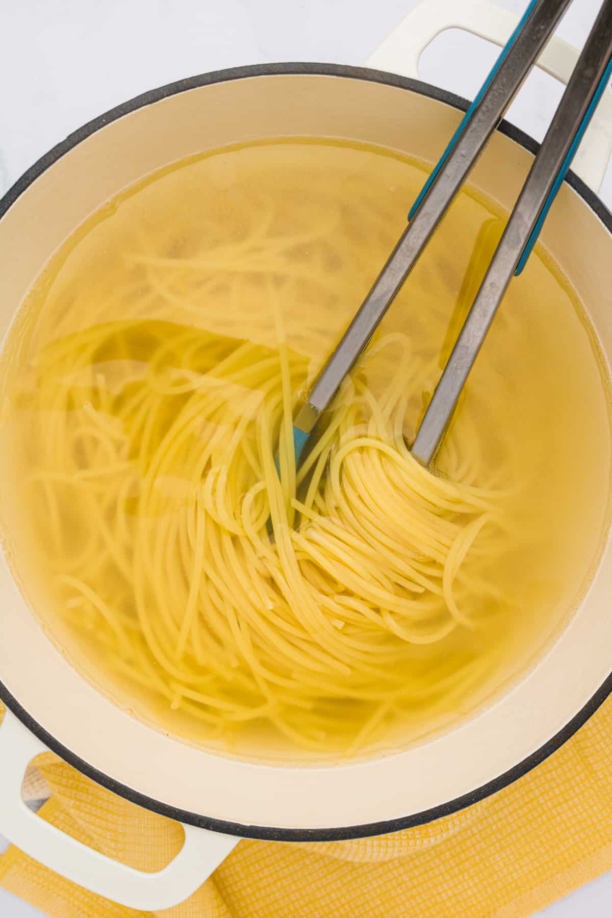 Spaghetti noodles in a 2-handled pot with tongs twirled into the noodles.