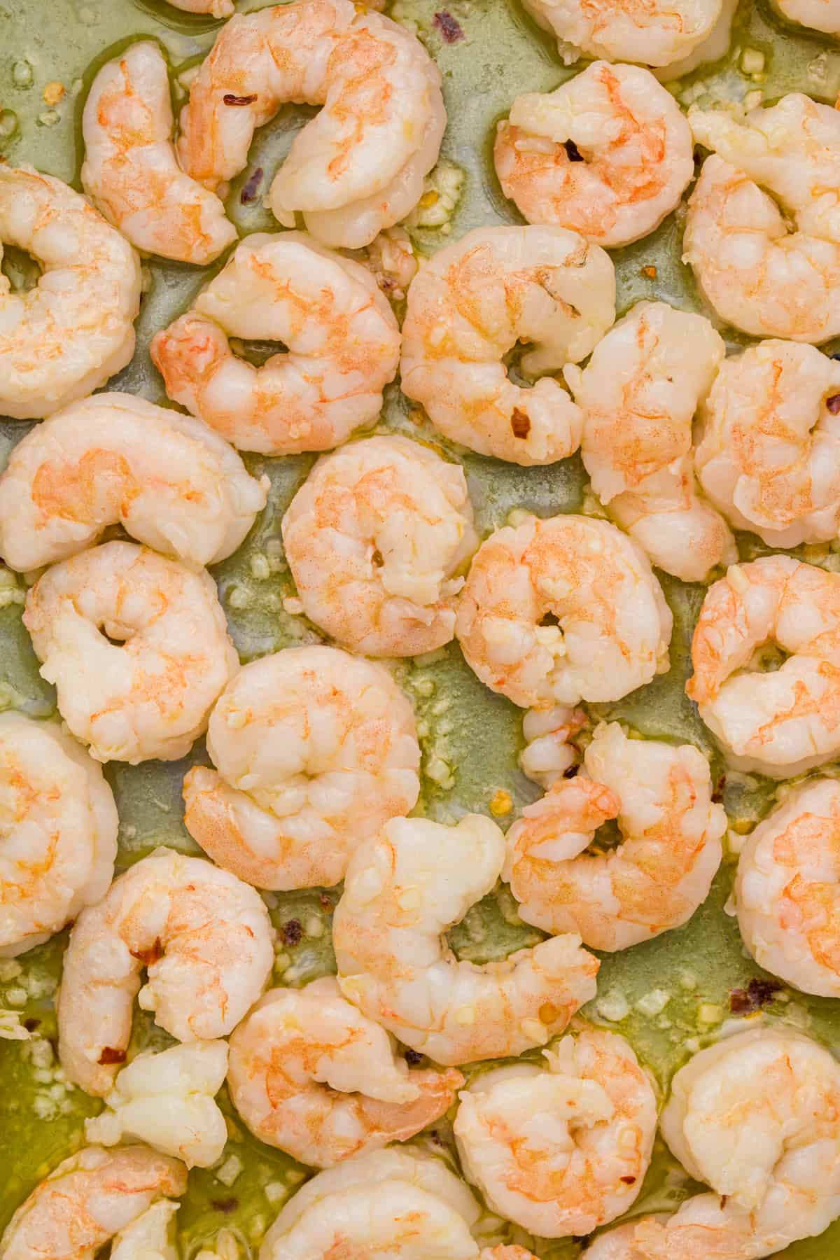 Shrimp cooking in oil and butter with minced garlic in a skillet.