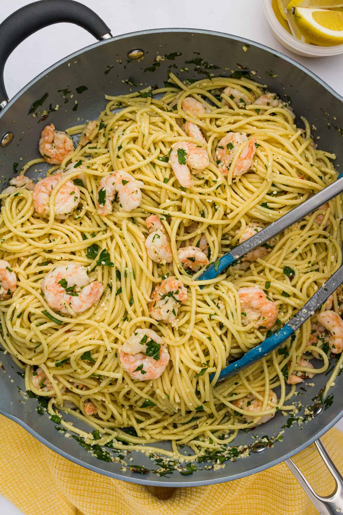 Spaghetti noodles and cooked shrimp being mixed with sauce, chopped parsley, and grated Parmesan in a skillet.