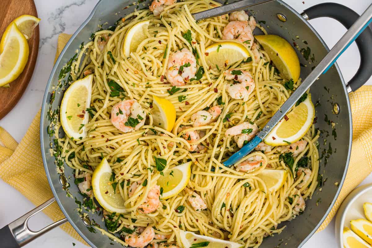 Overhead of Shrimp Scampi Pasta in a skillet with tongs twisted into the pasta and sitting on a yellow dish towel.