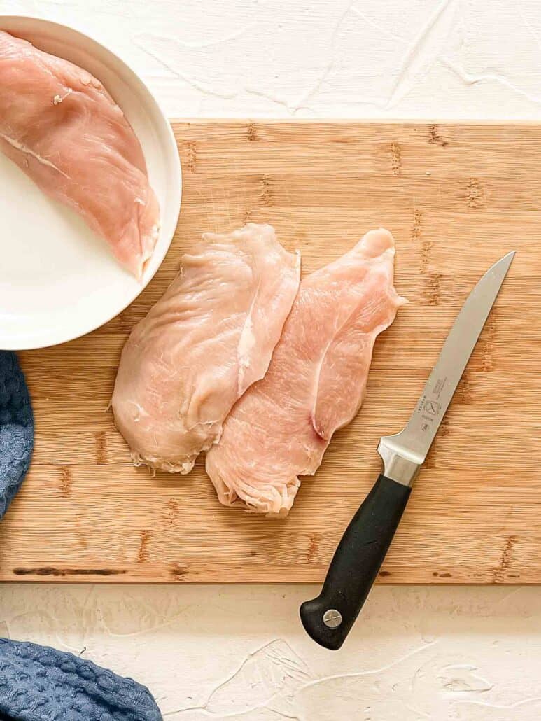 Raw chicken breast cutlets on cutting board with knife having been sliced in half lengthwise
