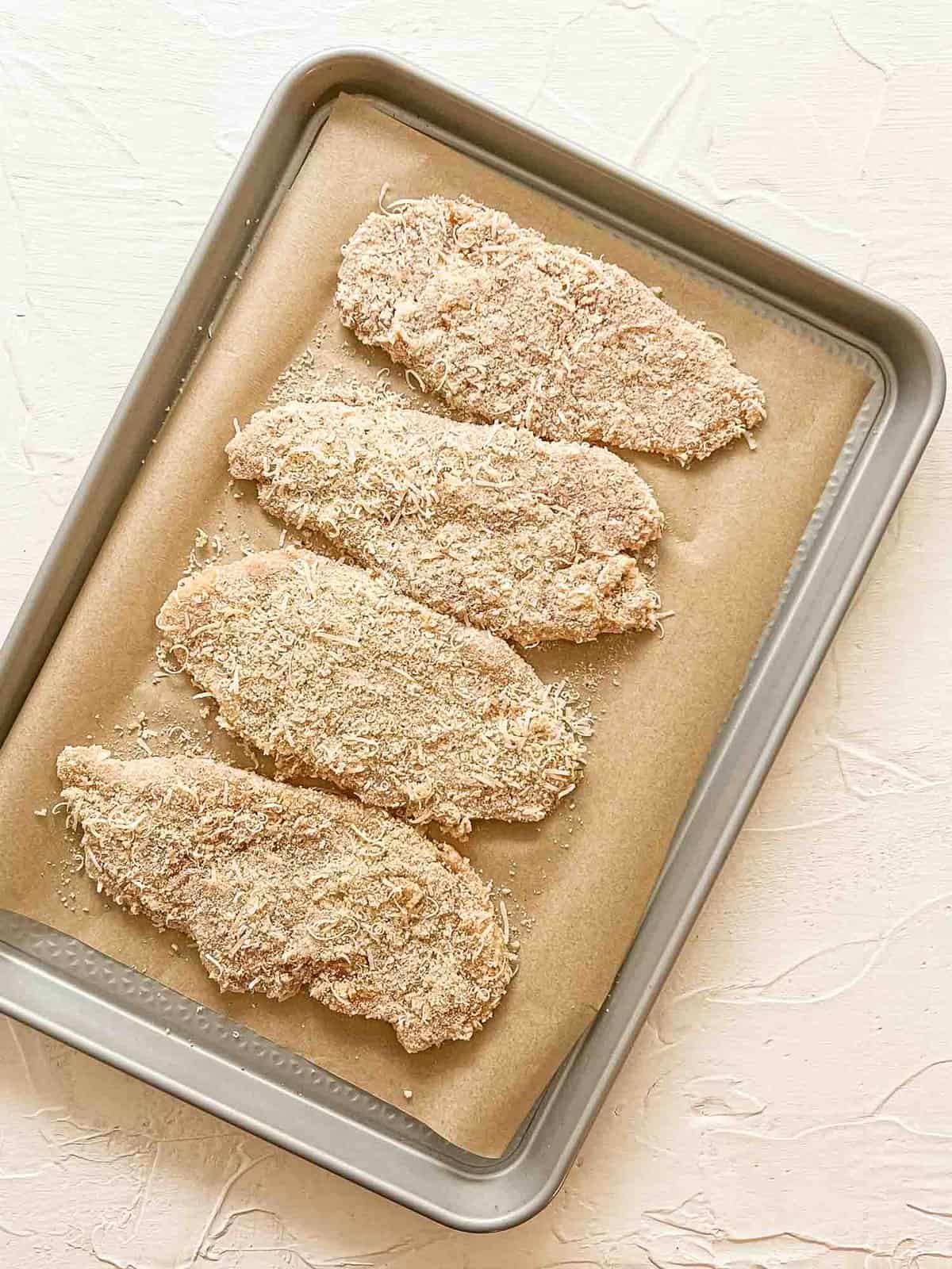 Raw breaded chicken breasts on baking sheet ready to be baked.