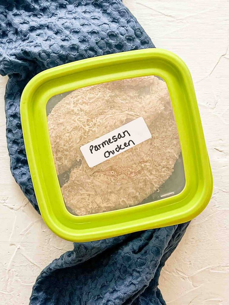 Breaded raw chicken breaksts in freezer container labeled Parmesan Chicken.