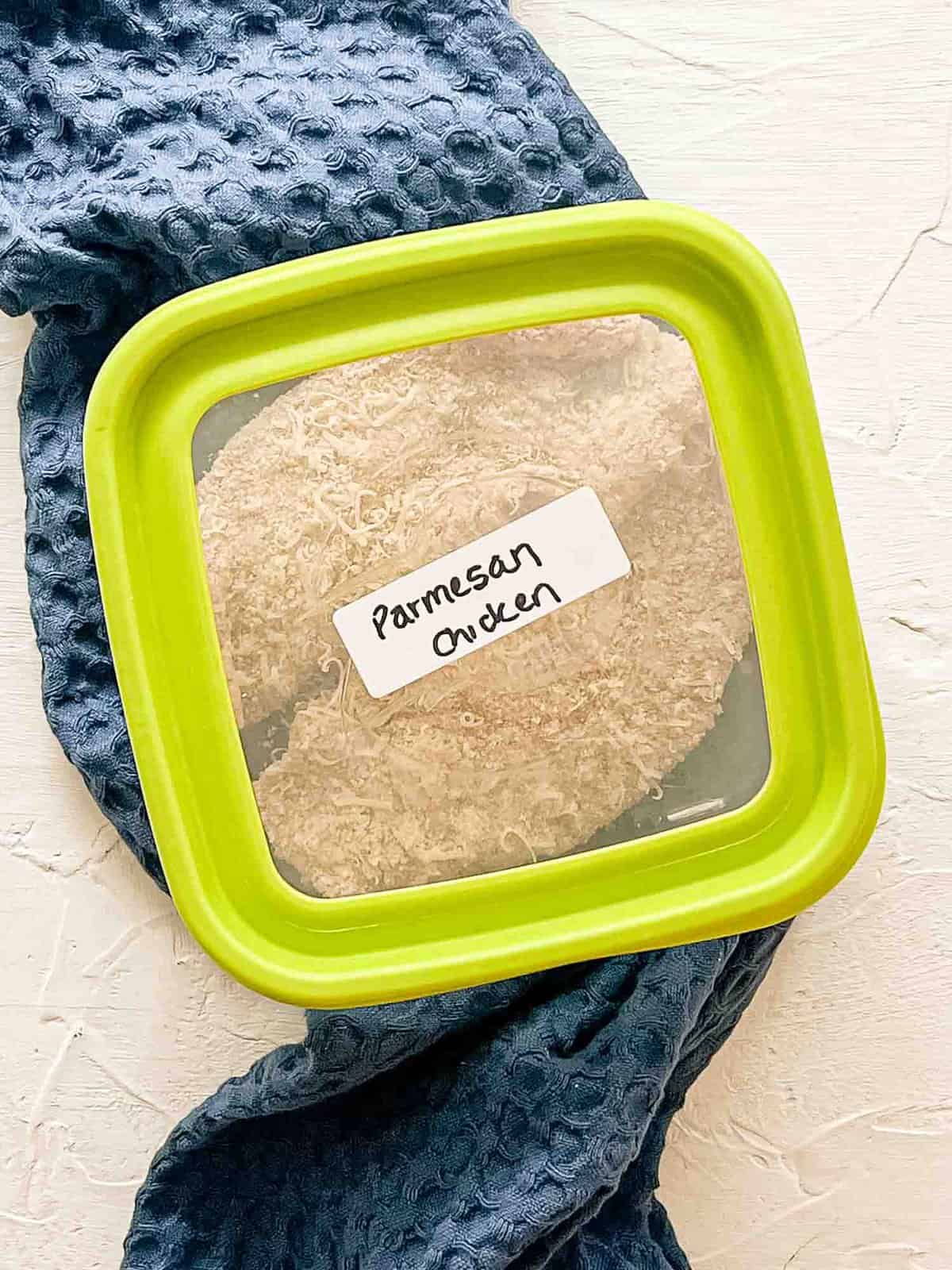 Breaded raw chicken breaksts in a freezer container labeled Parmesan Chicken.