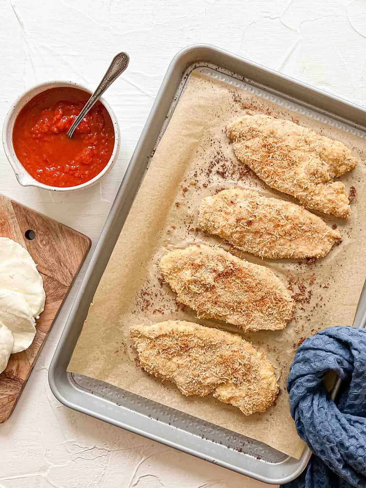 Breaded Chicken Breasts on baking sheet for Baked Chicken Parmesan.