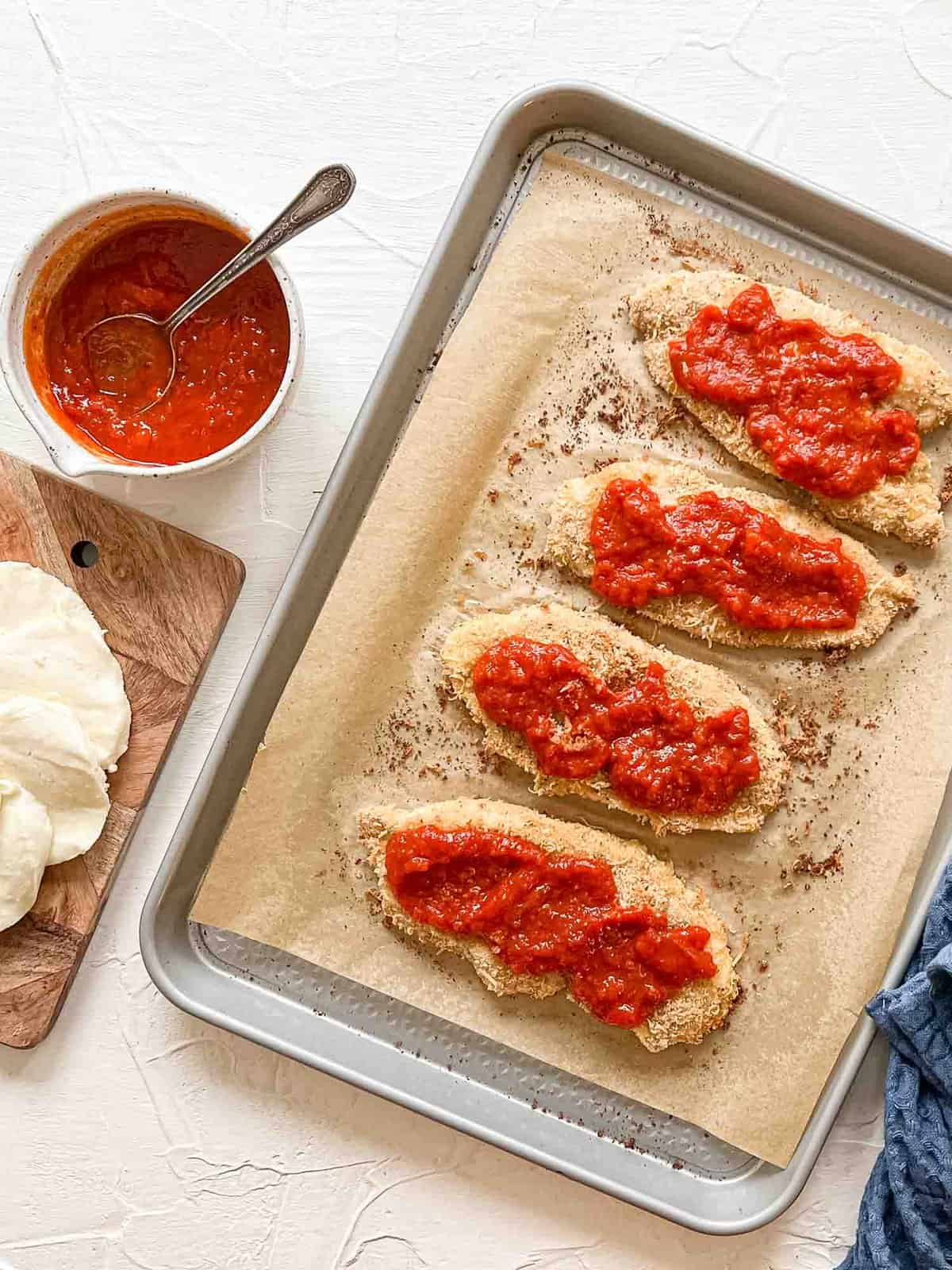 Breaded Chicken Breasts on baking sheet with marinara for Baked Chicken Parmesan