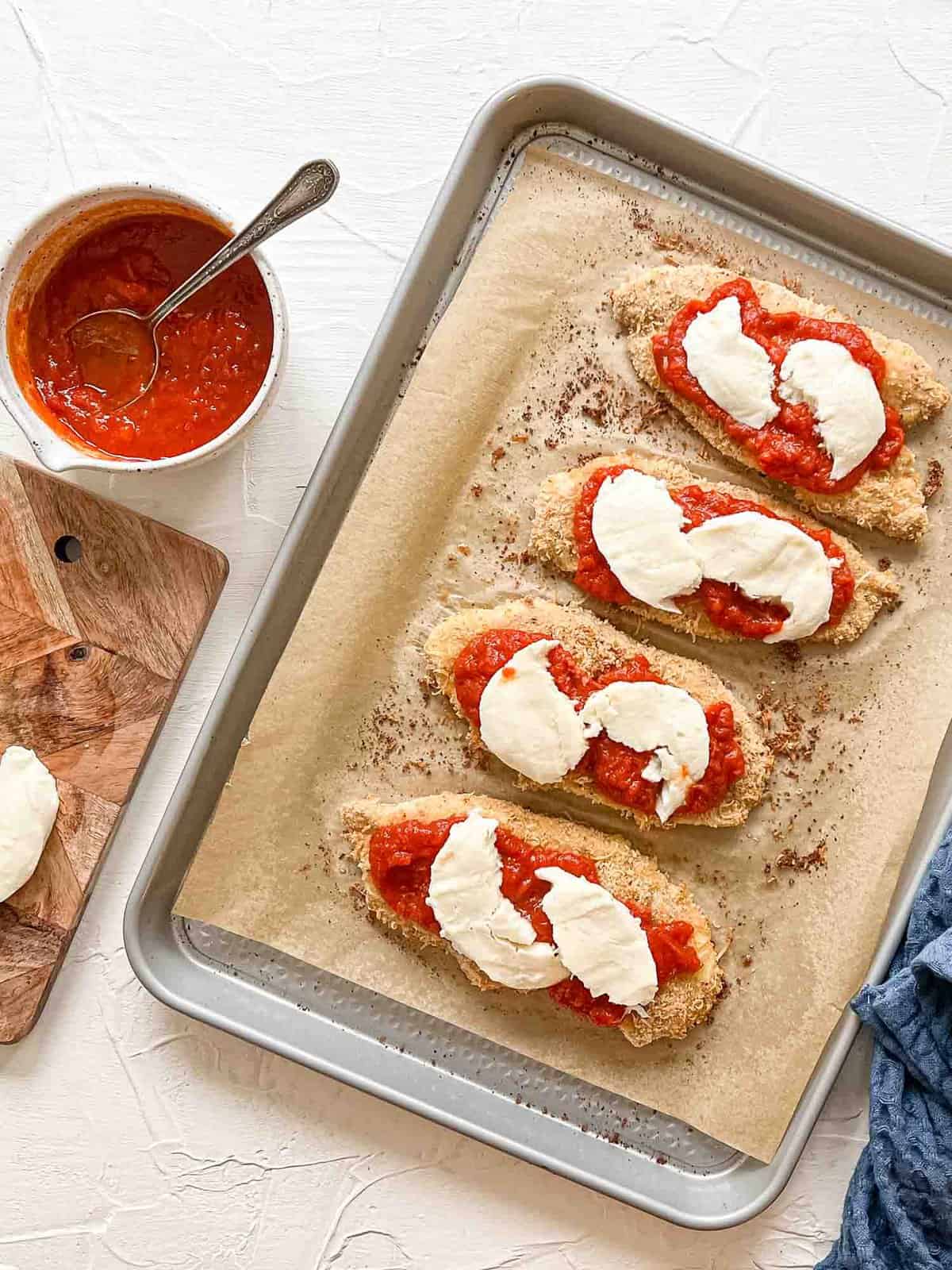Breaded Chicken Breasts on baking sheet with marinara and fresh mozzarella for Baked Chicken Parmesan