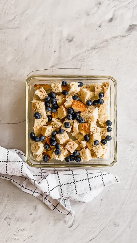 bread pieces and blueberries in a glass casserole dish with an egg mixture on top