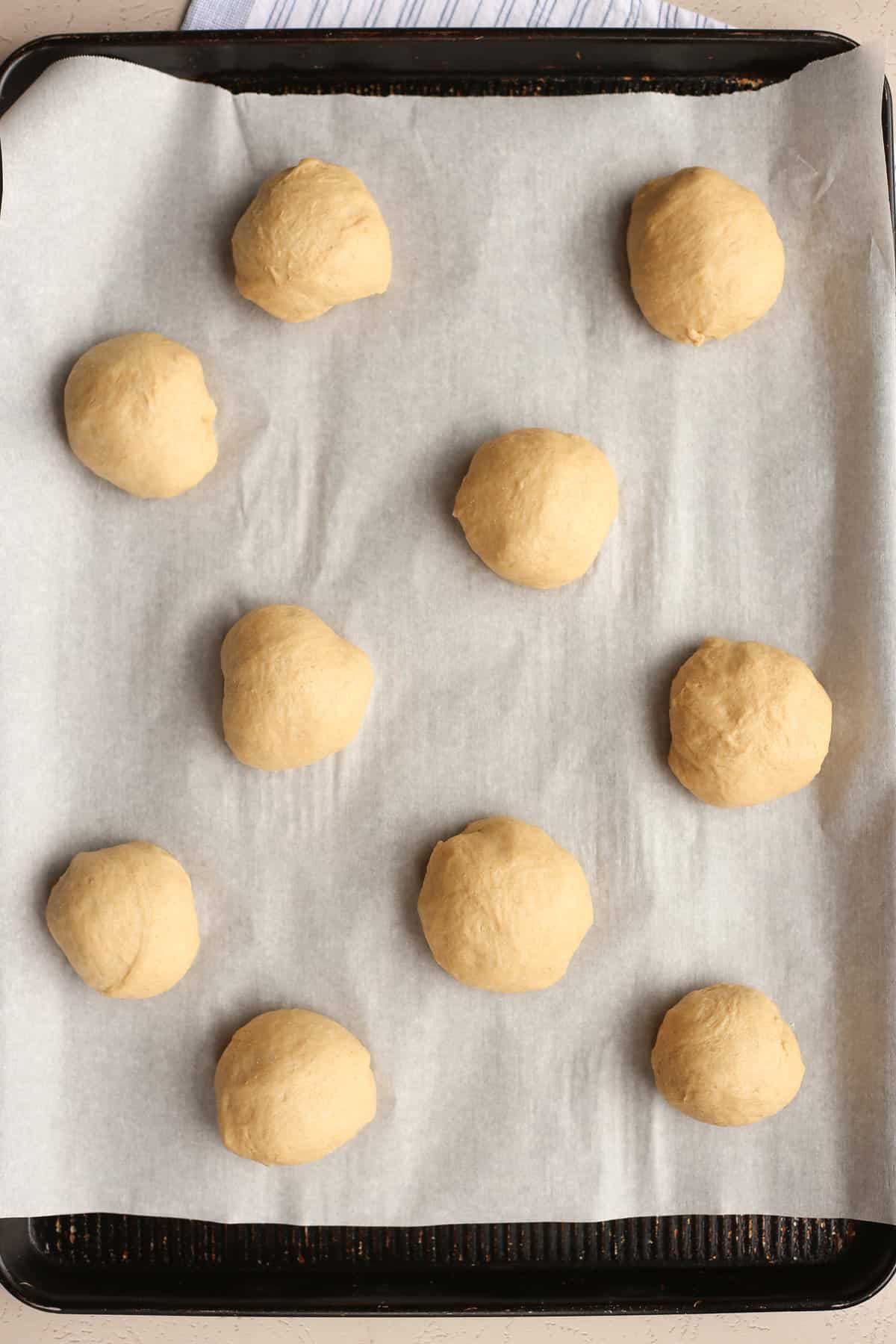 Whole Wheat hamburger bun dough rising on a parchment lined baking sheet.