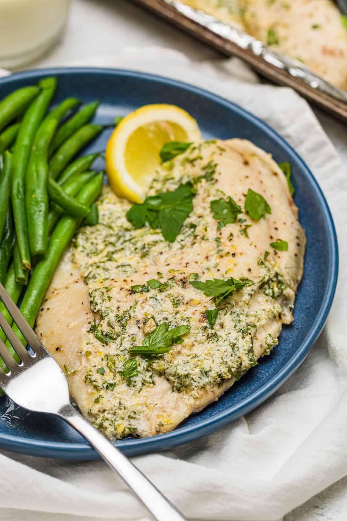 Parmesan Broiled Tilapia on a blue plate with long green beans and a fork.