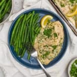 Parmesan Broiled Tilapia on a dark blue plate with long green beans and a fork on it as well.