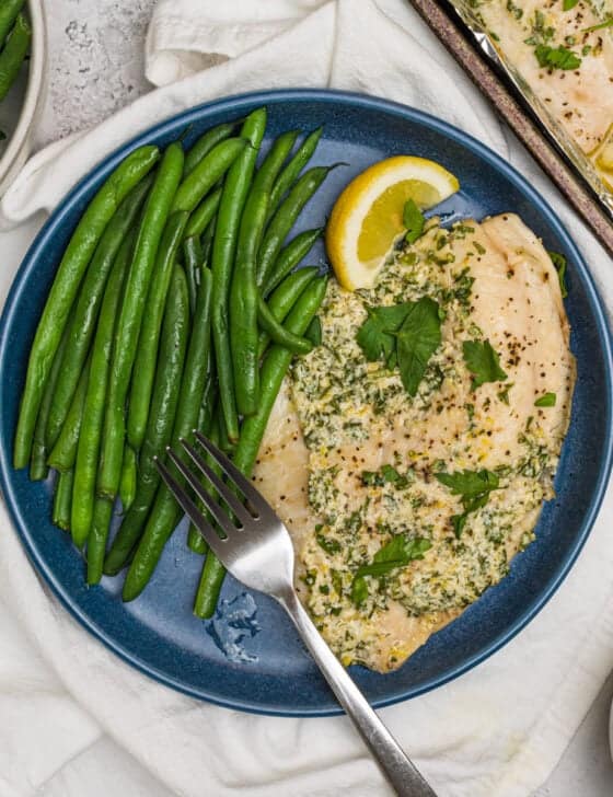 Parmesan Broiled Tilapia on a dark blue plate with long green beans and a fork on it as well.