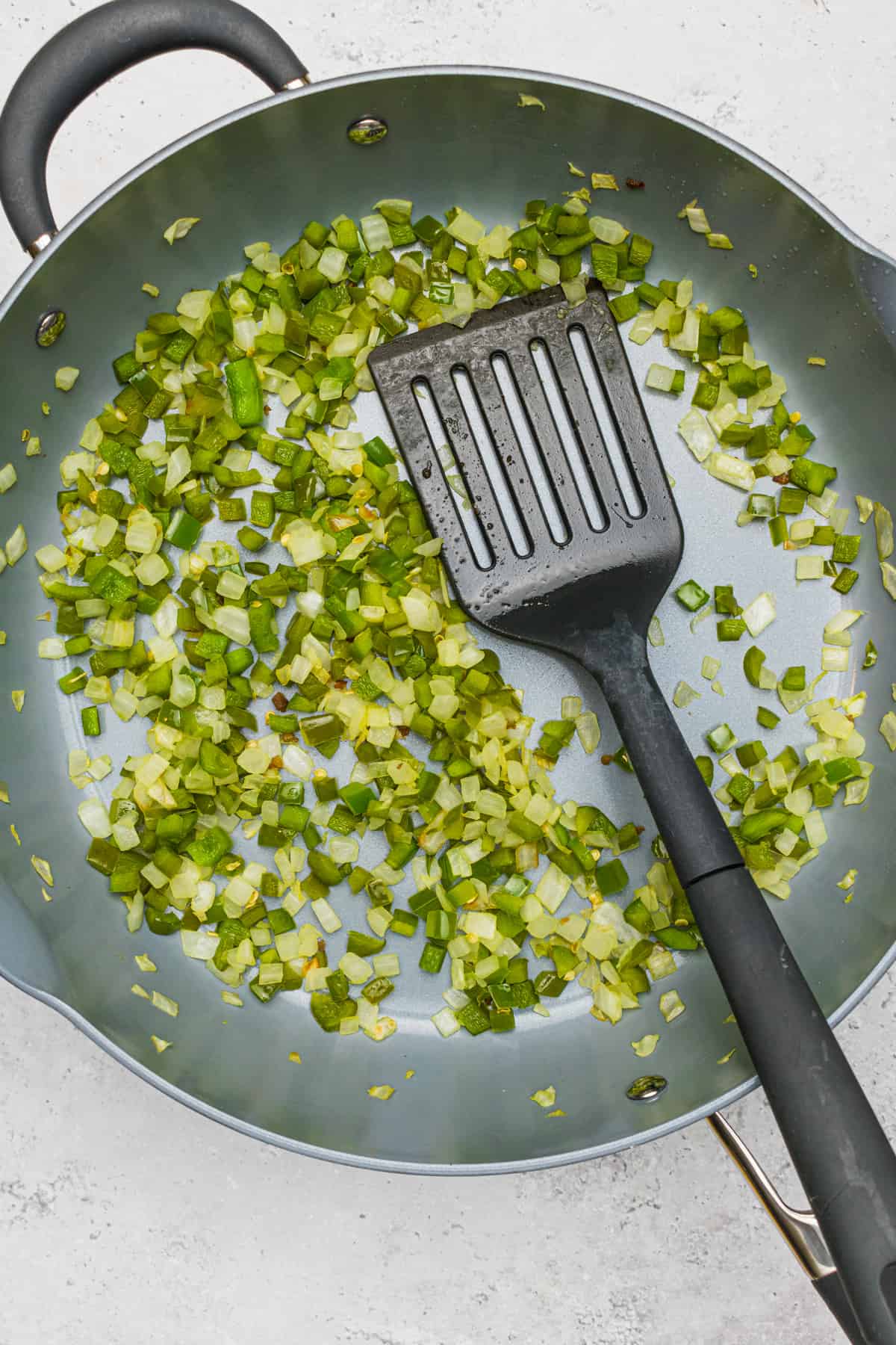 Chopped onions and green peppers sauteing in a skillet for Savory Breakfast Muffins.